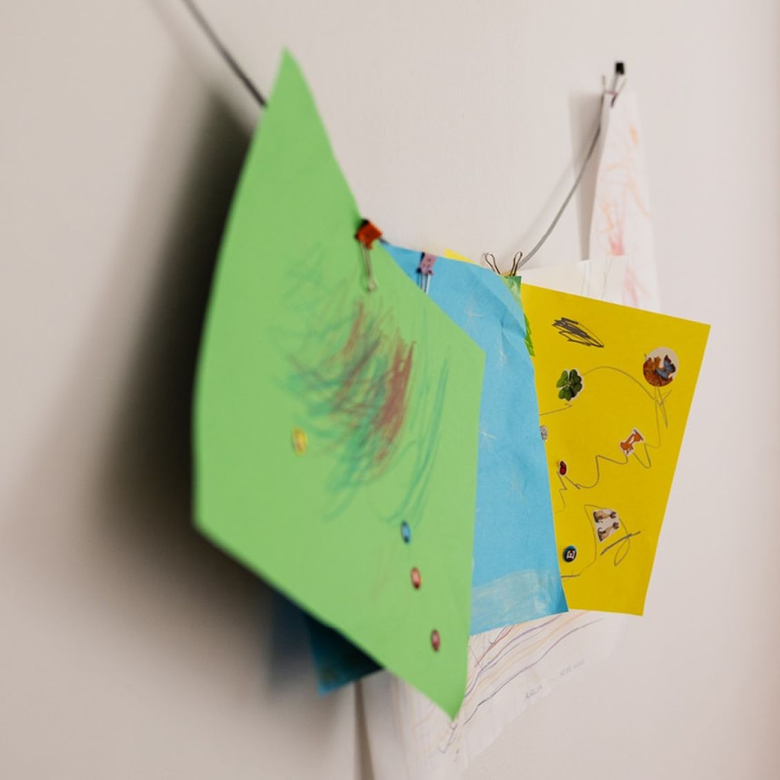 drei bunte Kinderzeichnungen h&auml;ngen an einer Wand