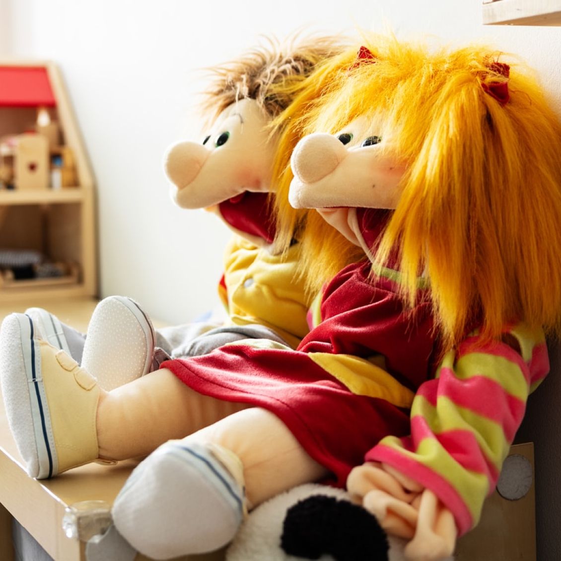 zwei bunte, stofferne Handpuppen mit fröhlichen Gesichtern sitzen auf einem Regal